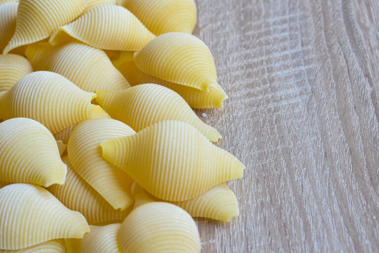 Detailed view of uncooked conchiglie pasta shells beautifully arranged on a textured wooden surface.